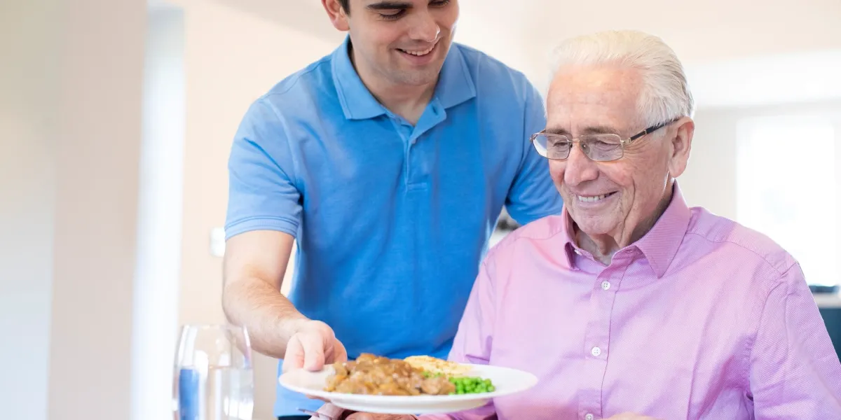 Man serving food to smiling elderly gentleman.