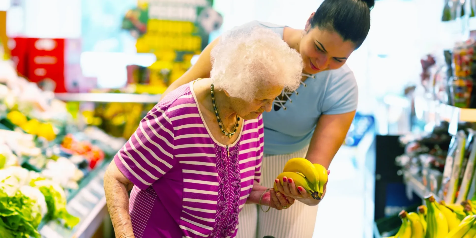 Woman assisting senior with banana selection.